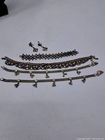 Overview photo showing five silver-tone bracelets and one pair of silver-tone square-patterned earrings all laid flat.