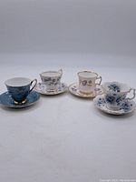 Front view of four English bone china tea cups and saucers with floral designs and gold trim.