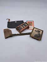 Overall view of the lot items showing WW2 U.S. muzzle cover, poker chips box, black pouch, and framed photo.