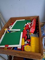 Wooden box filled with assorted vintage Lego bricks and two green baseplates visible