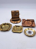 Overview of 5 vintage metal ashtrays in varied shapes and metal finishes.