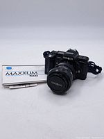 Full view of the camera with lens attached and instruction manual beside it on white background