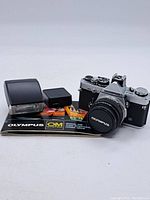 Full kit with Olympus OM-2 MD camera, flash unit, battery pack and manual displayed on white background.