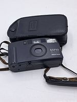 Front angle of the Pentax Espio AF Zoom camera with attached wrist strap and black leather carrying case in background.
