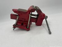 Side angle of the red metal vice showing the handle, jaw mechanism, and mounting base.