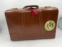 Front view of the vintage brown leather suitcase with 'WOLF ADVENTURE TOURS' sticker and red tassel on handle.