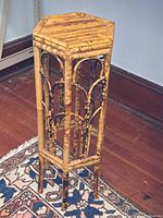 Full view of the hexagonal wooden end table showing bamboo or rattan lattice sides and slender legs on a wooden floor.