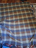 Full view of the wool blanket showing the plaid checkered pattern in blue, brown, tan and cream colors, spread out on a floor
