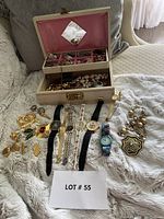 Full view of jewelry box open showing costume jewelry and watches arranged in front on fabric.