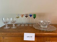 Front view of colorful liqueur stemware in assorted colors with two cut crystal goblets and cut crystal serving bowl with plate to the right.