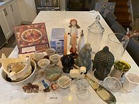 Wide view showing all decorative items arranged on a white table surface including bowls, figurines, jars, and candle warmer.