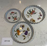 Photo of three ruffled edge Royal Worcester Evesham flan dishes displayed on a white surface showing their fruit designs and gold trim.