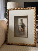 Framed antique powder flask in decorative gold frame with cream matting, shown from a distance