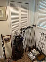 Golf clubs including woods, irons and a Callaway golf bag along with golf balls and golf decor set against a corner wall.