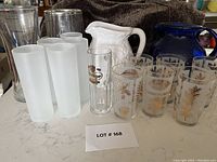 Photo of vintage and frosted drinking glasses, single tall glass with gold motifs, and two ceramic jugs in background