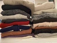Stack of folded sweaters and cardigans in various colors and knit patterns.