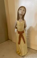 Front view of Lladro Naughty Girl figurine with detailed facial expression and yellow dress.