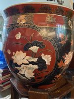 Close up of side showing lotus flower and floral design on reddish and black background with decorative band on top edge.