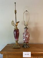 View of two vintage decorative lamps side by side on wooden surface with a plain wall background.