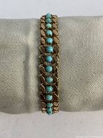 Bracelet displayed on a cylindrical pillow showing gold links and turquoise stones