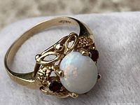 Close-up top view of ring showing oval opal cabochon and two round rubies in the decorative gold setting