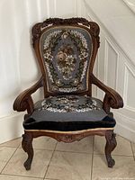 Full front view of the carved wooden armchair with upholstered seat and back