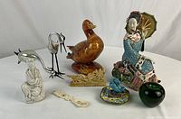 Overview image showing all items in the collection including ceramic duck, porcelain maiden, silver cranes, dragon engraved spoon, Guanyin figure, blue bird on floral base, and green pot
