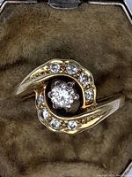 Close-up top view of ring showing central diamond and surrounding pavé diamonds.