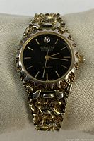 Front view showing black dial with Gruen logo, diamond accent and goldtone bezel and bracelet.