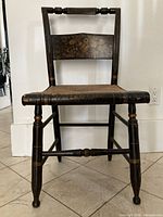 Front view of antique Hitchcock chair showing hand-painted fruit stencil design on backrest, painted wooden frame with turnings and woven seat.