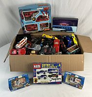 Full lot view showcasing boxed sets and loose toy cars inside a cardboard box