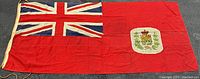 Full view of red cotton flag with Union Jack canton and printed coat of arms, showing entire flag and rope halyard