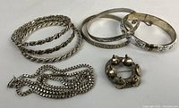 Overview of three bracelets, box chain necklace, and circular brooch on white background