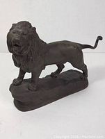 Side angle view of metal lion statuette showing full body, rock base, and curled tail.