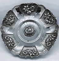 Top view of the round silver bowl showing scalloped edge and floral decorations around the rim with a central ship motif.
