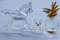 Three crystal figurines arranged in a row: rocking horse on left, bear in middle, pineapple on right, all on white background