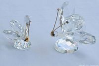 Two Swarovski crystal butterfly figurines shown from a side angle, displaying faceted clear crystal wings and bodies with gold antennas and black eyes, mounted on faceted round crystal bases.