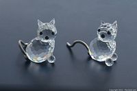Clear faceted Swarovski crystal mini cat figurines with metal coil tails viewed on dark background.