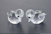 Two clear, faceted Swarovski crystal duck figurines on black background, showing overall shape and detail of ducks swimming with black eyes and raised tails.