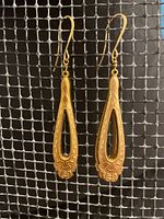 Pair of brass Art Nouveau earrings shown from front on a metal mesh background.