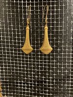 Pair of brass Art Nouveau earrings wire wrapped on gold plated earwires shown hanging against a mesh background