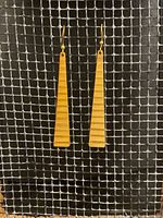 Photo of pair of long triangular brass tipi earrings with gold plated ear wires displayed on a dark mesh background. Each earring has two tipi shapes with horizontal grooves giving an Art Deco style.