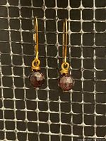 Pair of wire wrapped garnet drop earrings with gold plated ear wire displayed on a metal mesh background.