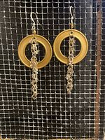 Photo showing a pair of handmade earrings with drilled brass hoops and attached silver plated chains on silver plated ear wires. Background mesh grid.