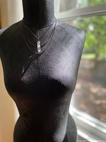 Full view of the quartz crystal pendant necklace displayed on a black mannequin torso against window light showing overall length and layering effect of the oxidized chains.