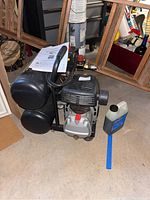 Full view of the black Central Pneumatic twin tank air compressor, showing air tanks, motor, handle, oil bottle, and instruction manual nearby.