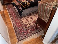 View of one side of the Oriental area rug laid on hardwood floor showing red floral border and central cream pattern with floral medallions.