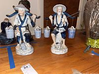 Both figurines side by side on tabletop with auction tag visible