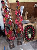 Two cone-shaped berry trees on bases decorated with various colored berries and leaves, alongside a Christmas wreath with red apples and pineapple inside a cardboard box.