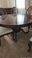 Side view of round wooden dining table showing claw foot base and part of chairs